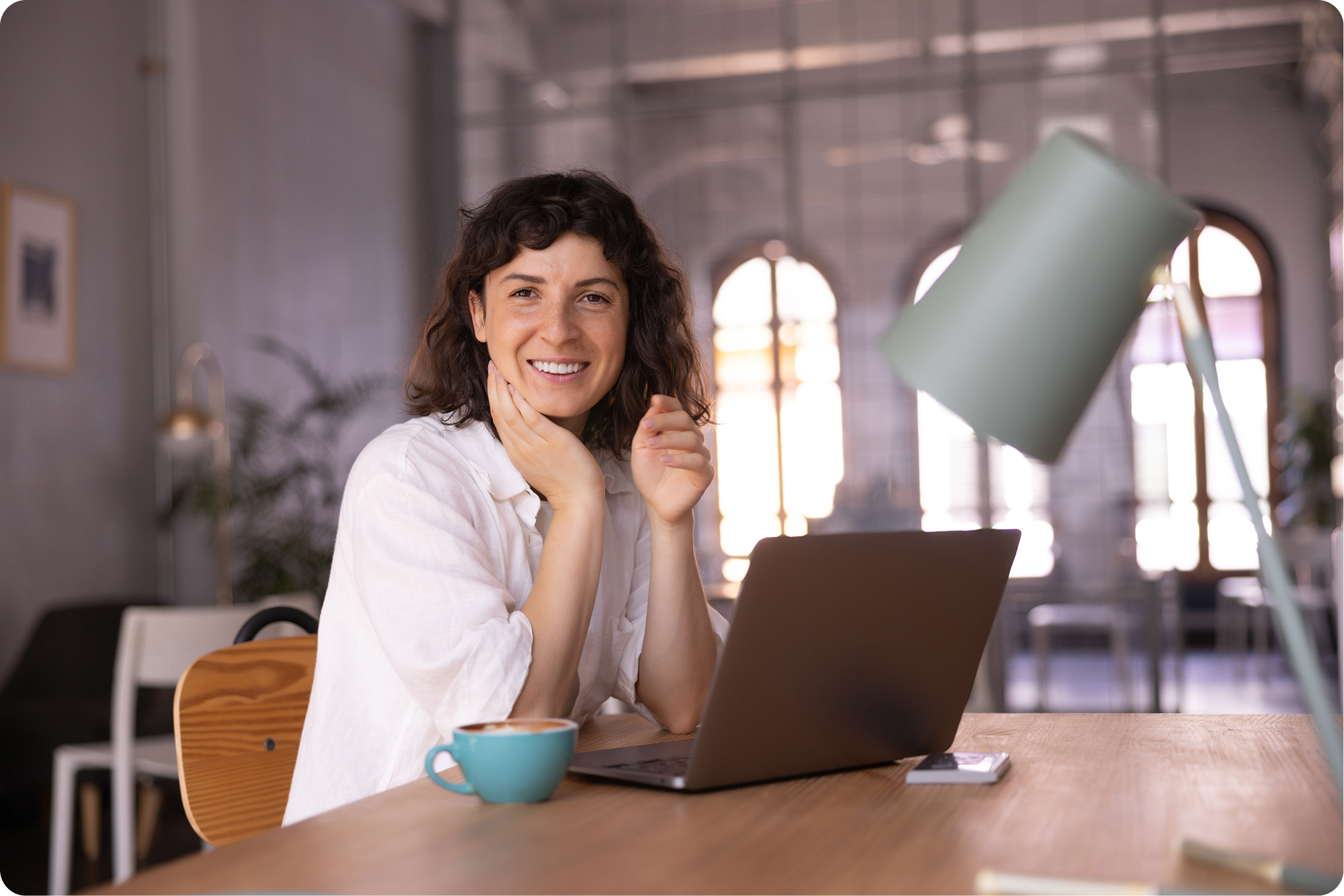 chica-morena-caucasica-joven-positiva-mirando-la-camara-sentada-en-la-mesa-con-la-computadora-portatil-en-el-interior 1